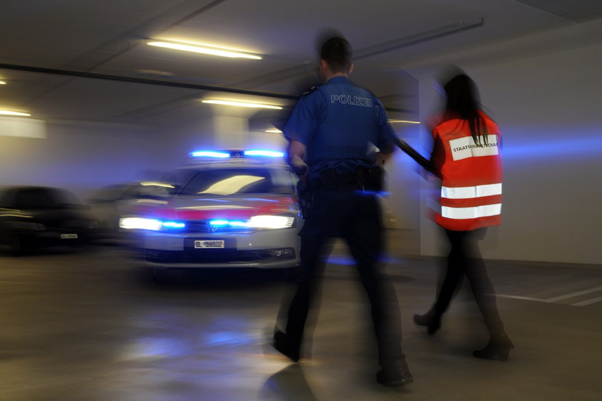 Eine Mitarbeiterin der Staatsanwaltschaft und ein Mitarbeiter der Polizei Basel-Landschaft sind gemeinsam im Einsatz. Im Hintergrund steht ein Fahrzeug der Polizei.